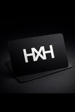 Honor The House Gift Card with HXH badge logo in white on black card with grey/black background. Card leans on a slight angle.