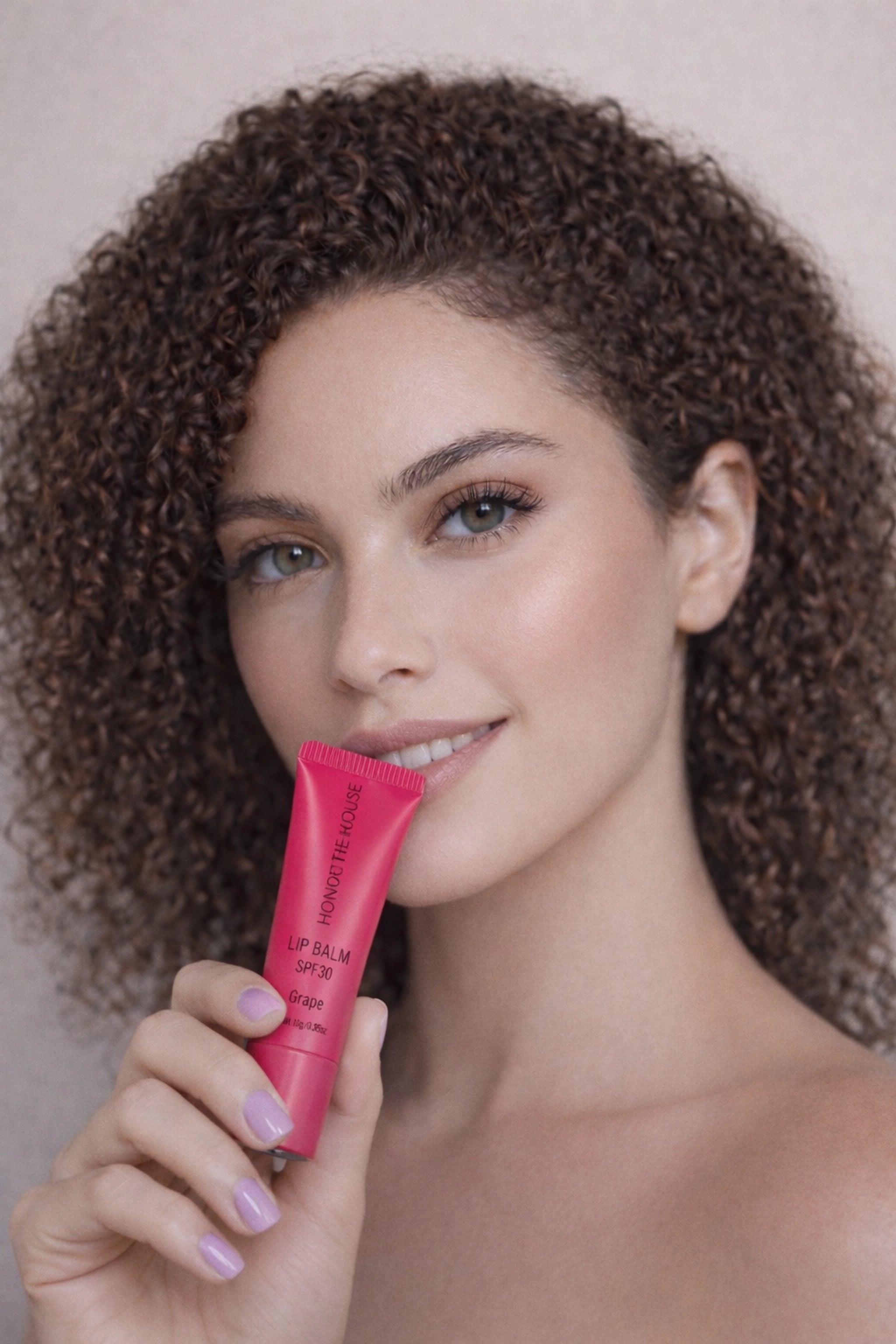 Honor The House SPF 30 Lip Balm in Cabernet Grape being held by light skin model with curly hair.