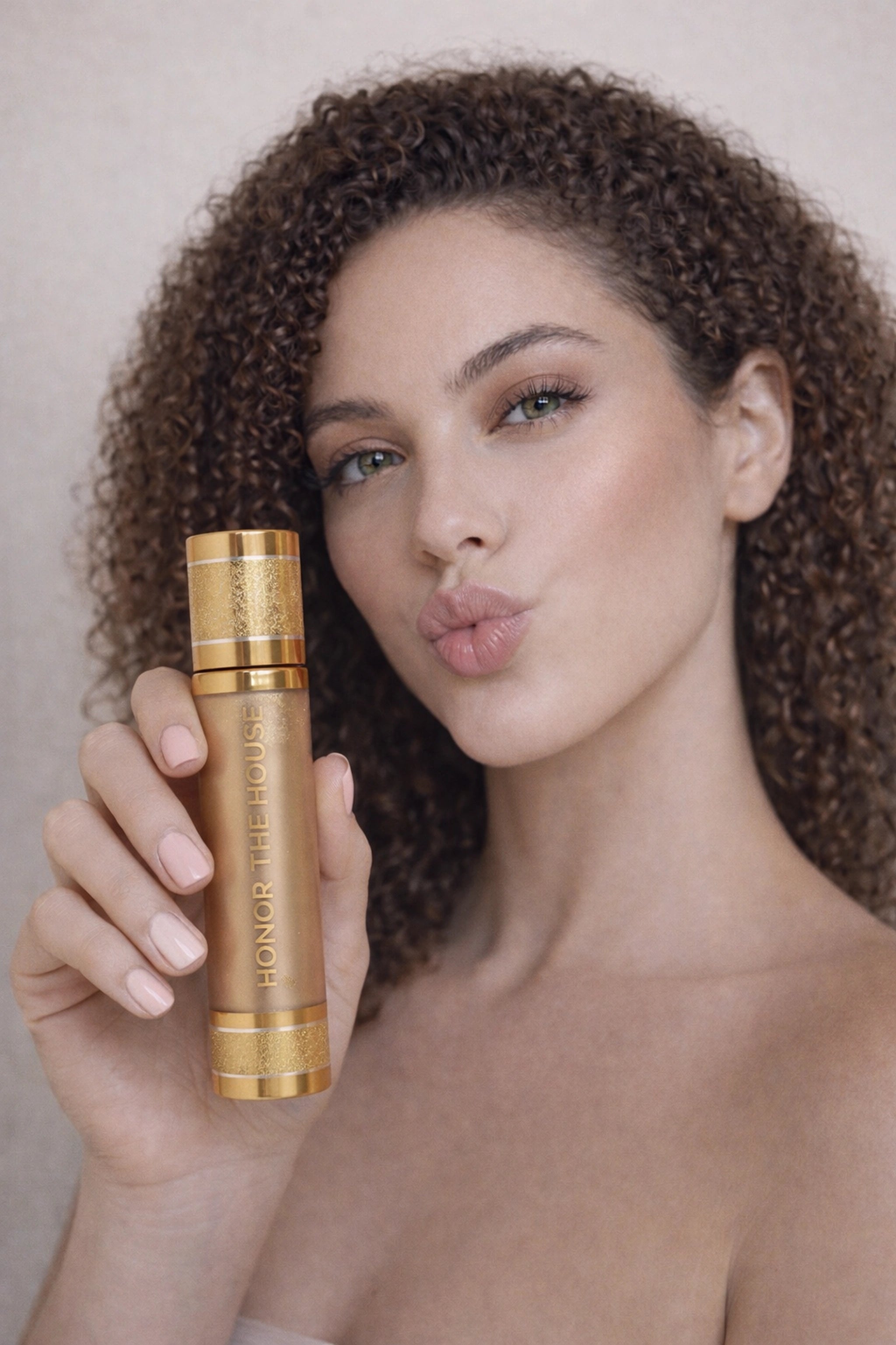Honor The House Drippin' Gold Liquid Highlighter in Honey Soft Glow on display on a model's cheek and holding product tube in right hand.