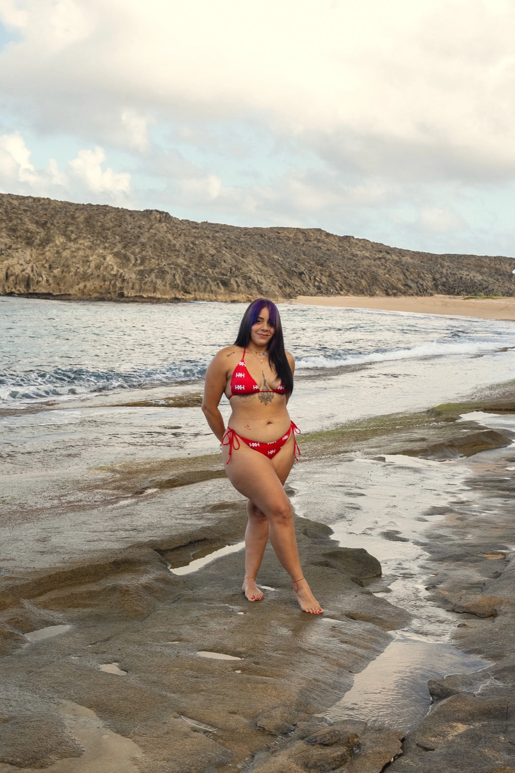 Model wearing Honor The House Breeze Off The Ocean Bikini in Caribbean Cherry colorway in a beach cove.