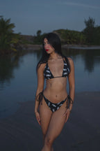 Model wearing Honor The House Breeze Off The Ocean Bikini in Umbreon Black Color at shore during the night looking to her right