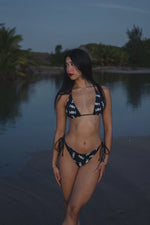 Model wearing Honor The House Breeze Off The Ocean Bikini in Umbreon Black Color at shore during the night looking to her right